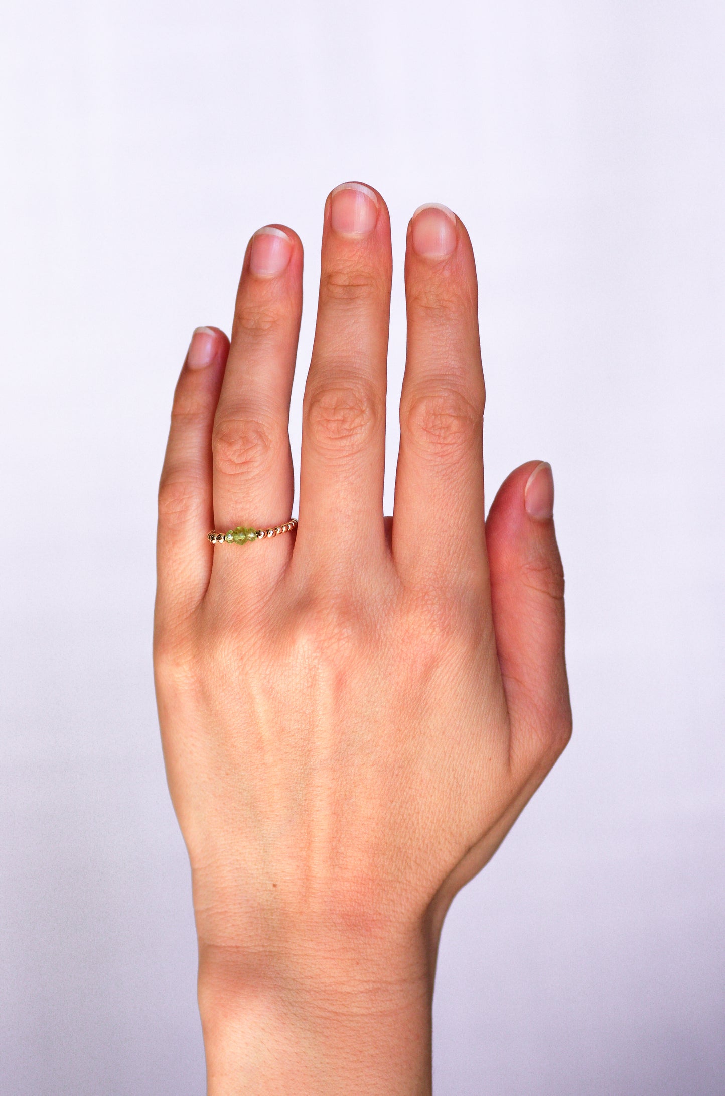 Minimalist beaded ring with faceted peridot and gold beads, worn on a hand, showcasing elegant and delicate design