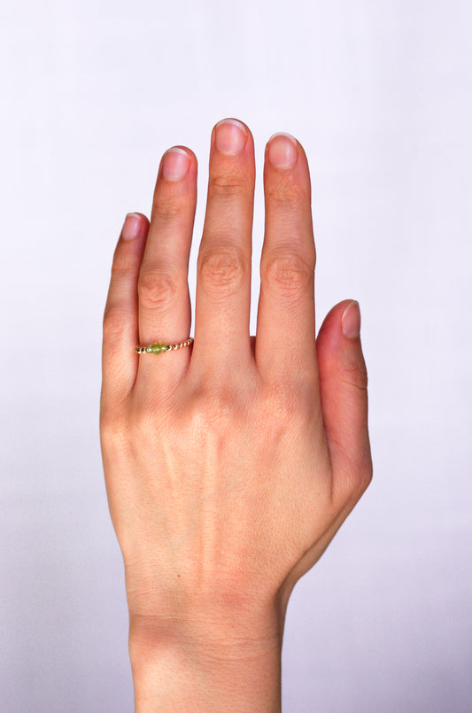 Minimalist beaded ring with faceted peridot and gold beads, worn on a hand, showcasing elegant and delicate design