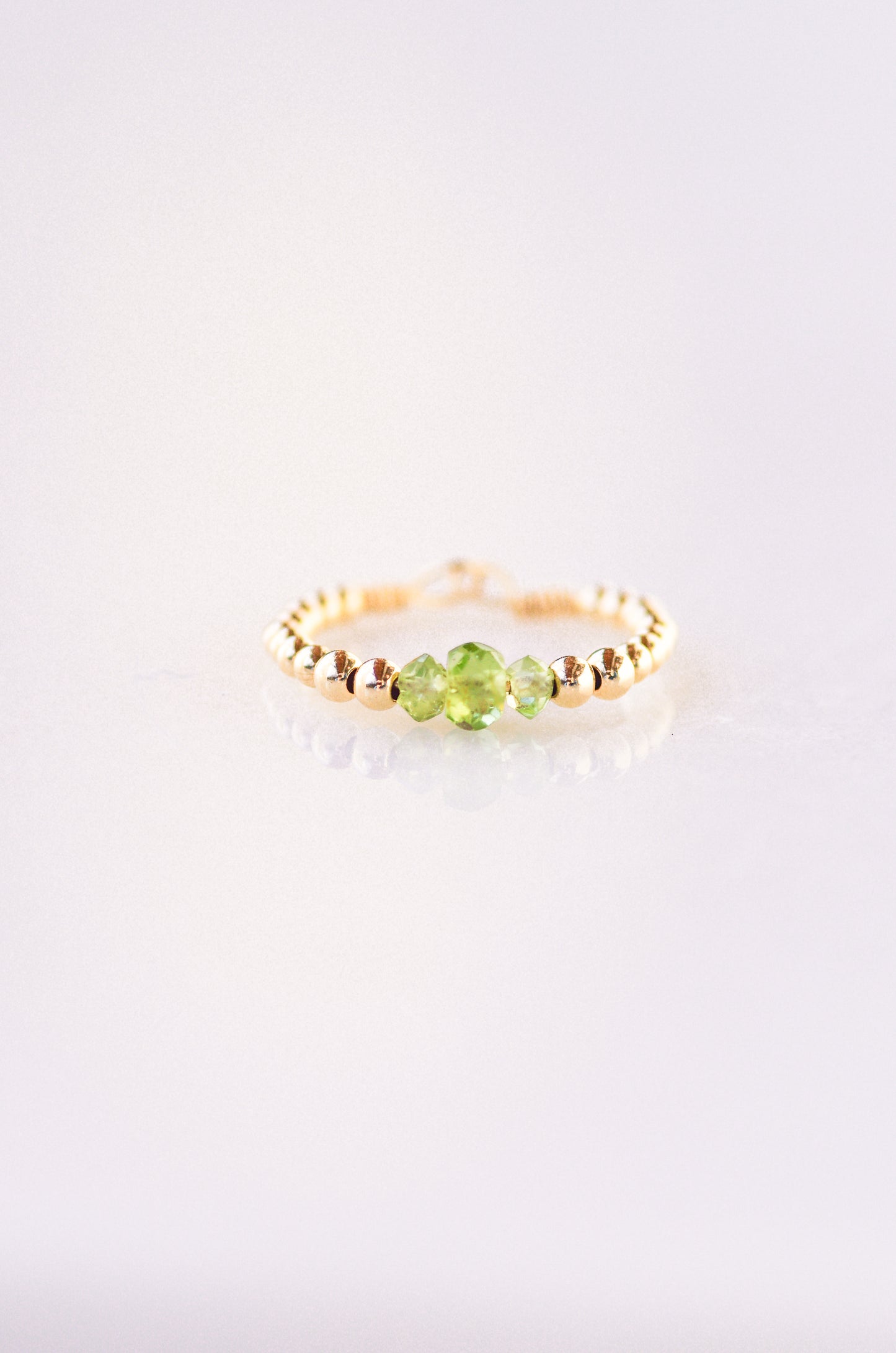Minimalist beaded ring with faceted peridot and gold beads, showcasing elegant and delicate design