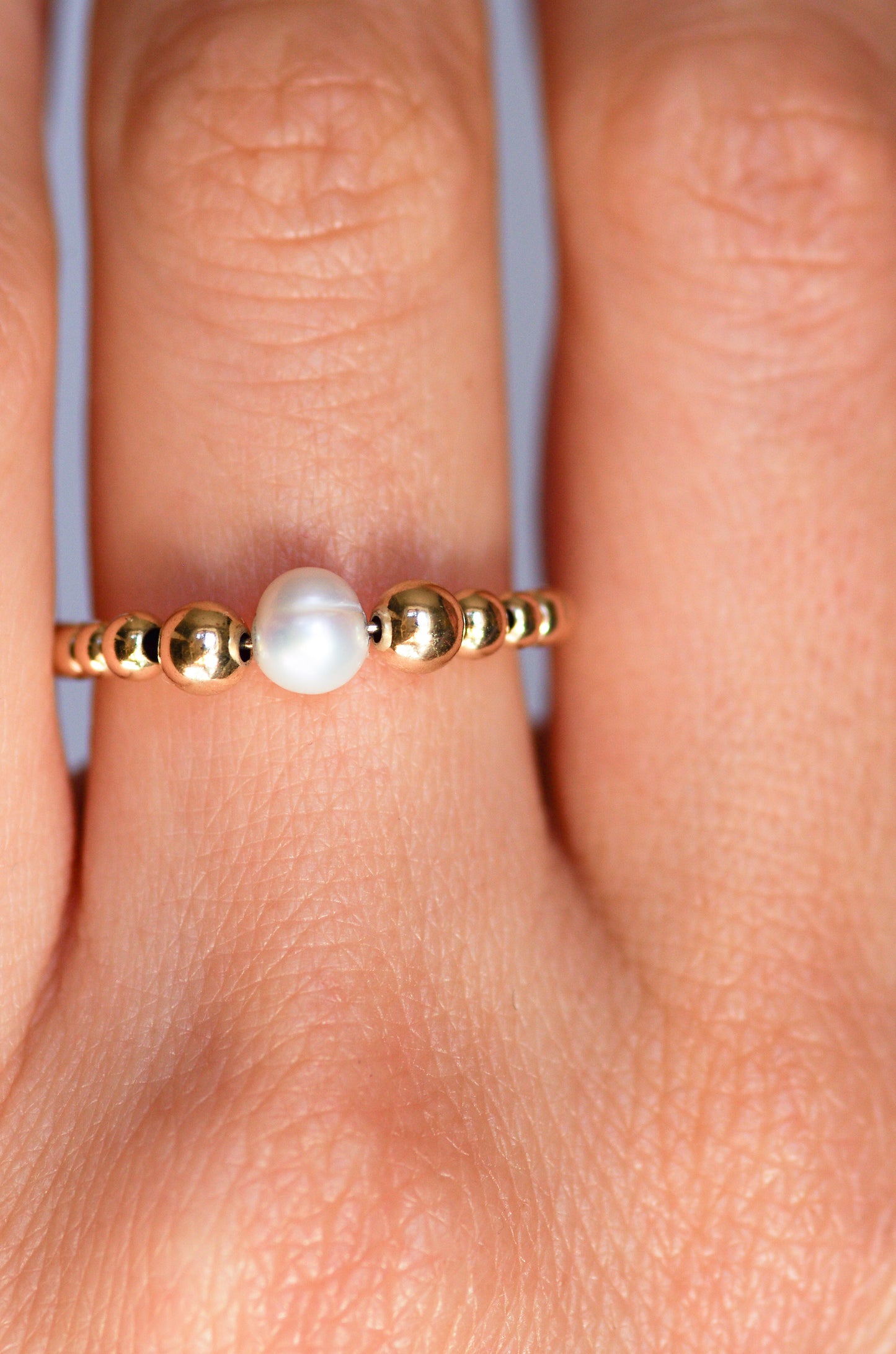 Delicate ring featuring a central irregular pearl and graduated gold beads, worn on a hand to showcase its refined and organic elegance.
