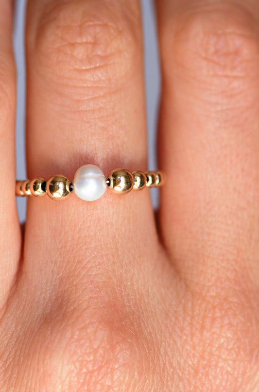 Delicate ring featuring a central irregular pearl and graduated gold beads, worn on a hand to showcase its refined and organic elegance.