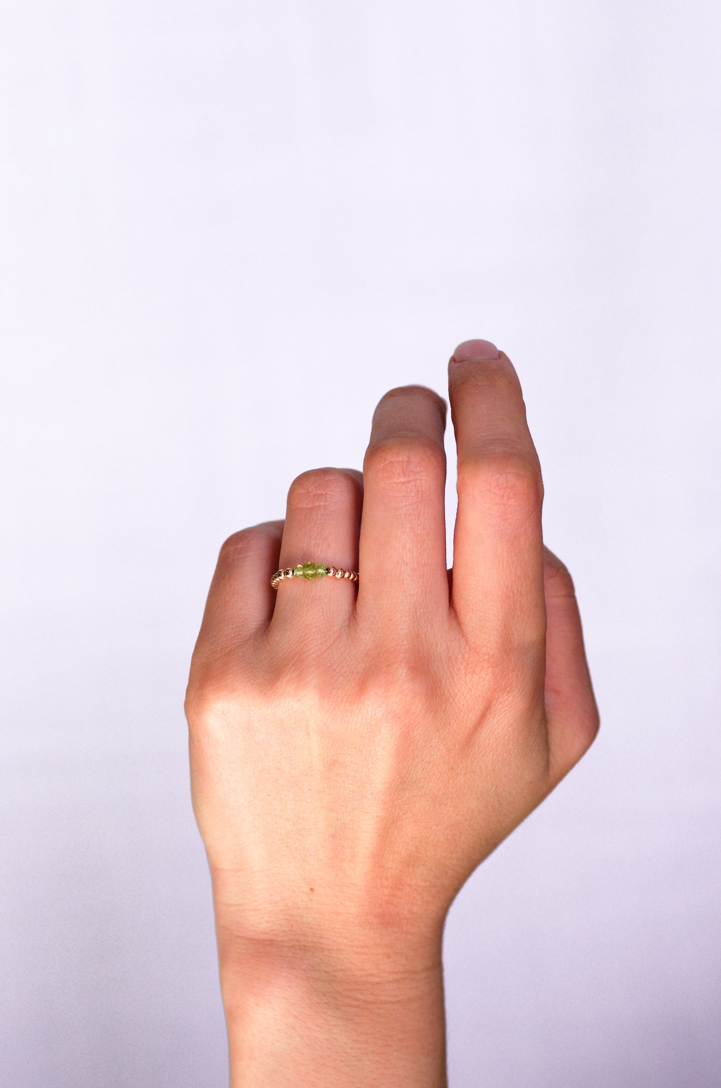 Beaded ring with faceted peridot and gold beads, worn on a hand, showcasing elegant and delicate design