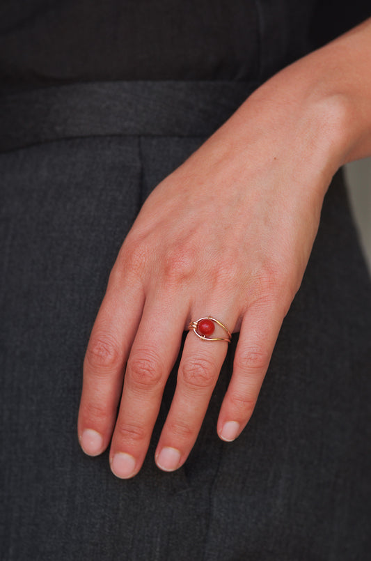 Hand wearing a sustainable ring with a red coral against a dark background