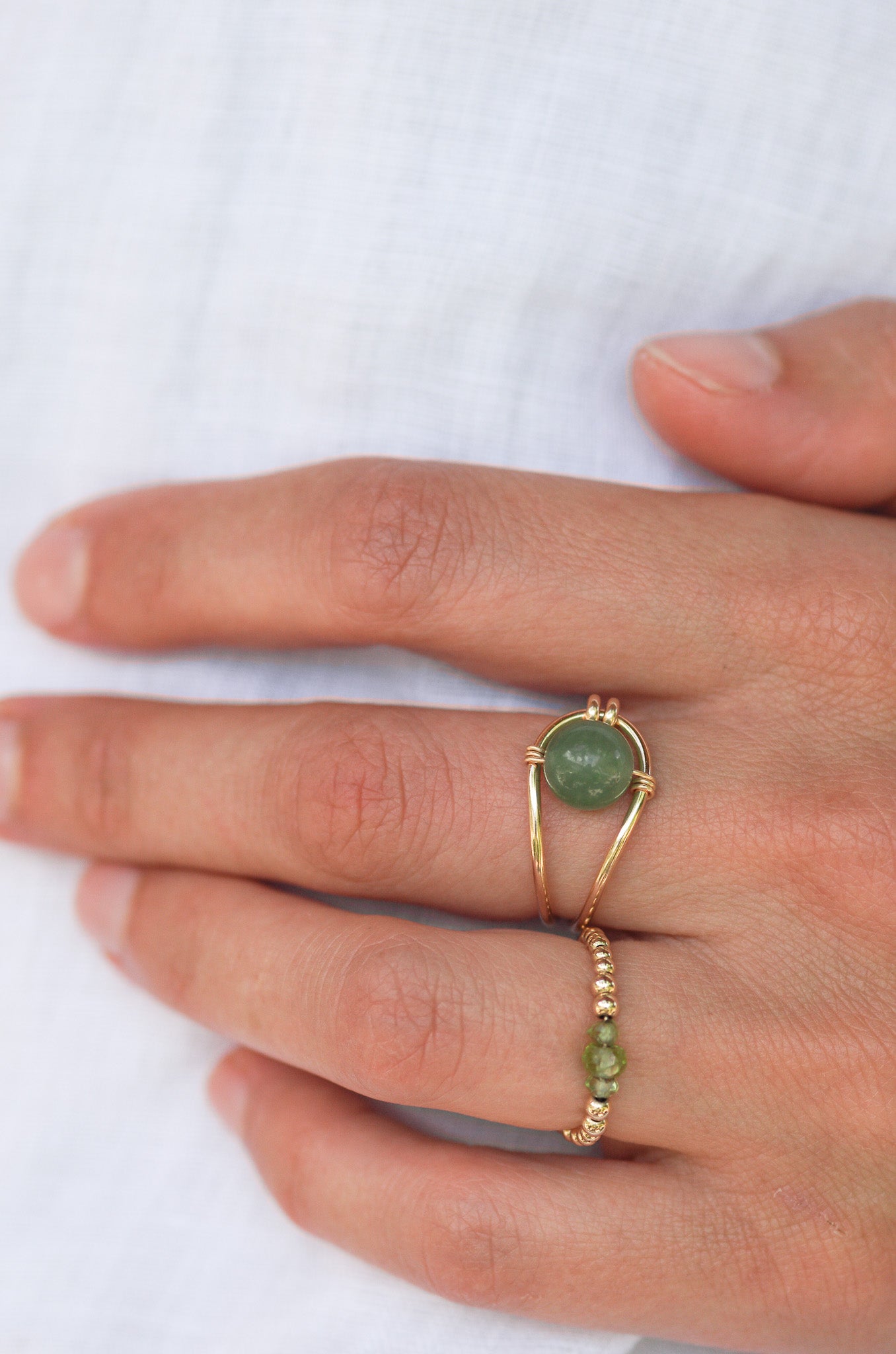 two Sustainable Gold rings with green gemstones on a hand against a white background