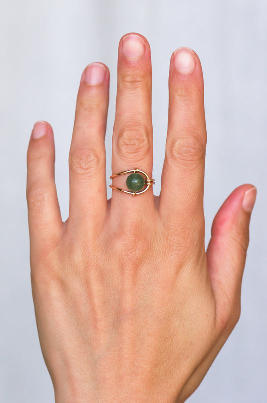 Hand wearing a sustainablering with a green gemstone on a light gray background