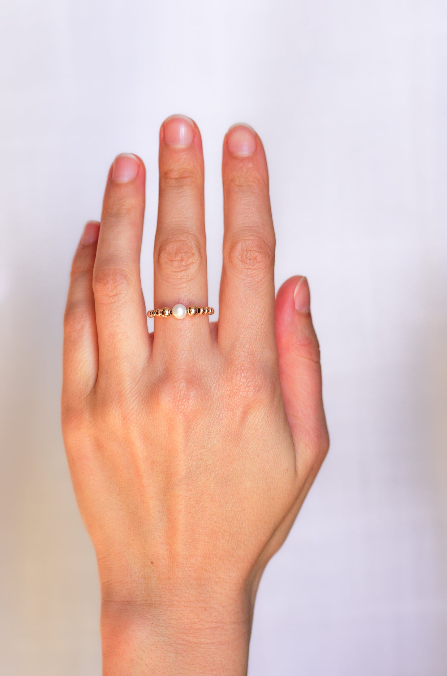Delicate ring featuring a central irregular pearl and graduated gold beads, worn on a hand to showcase its refined and organic elegance.