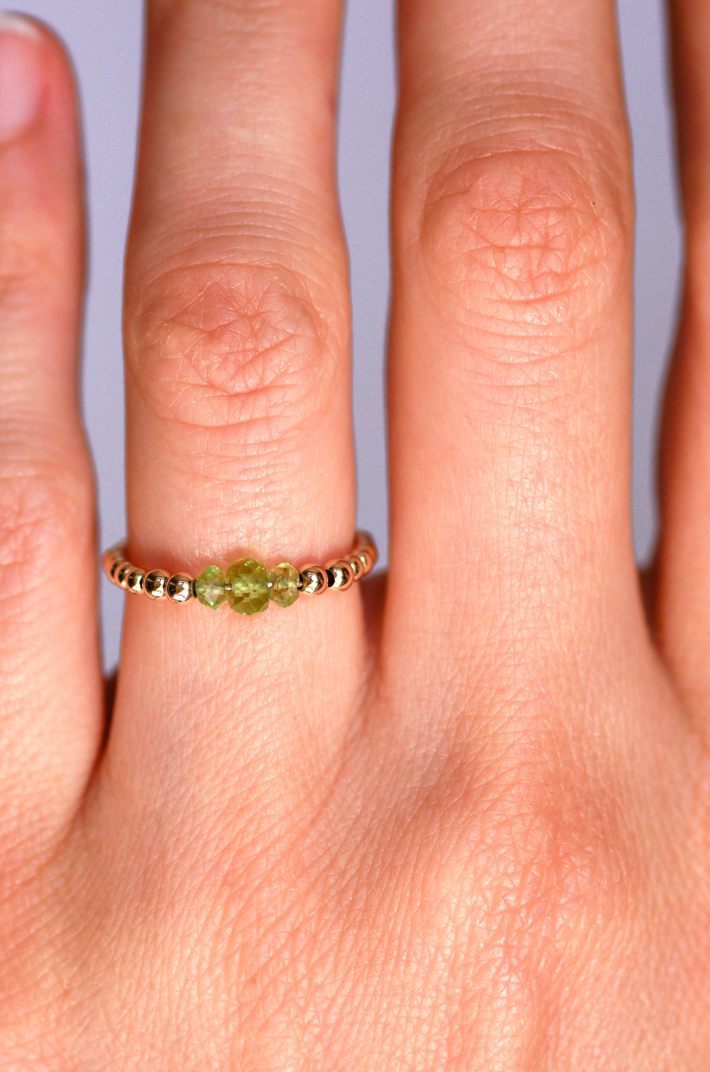 Minimalist beaded ring with faceted peridot and gold beads, worn on a hand, showcasing elegant and delicate design