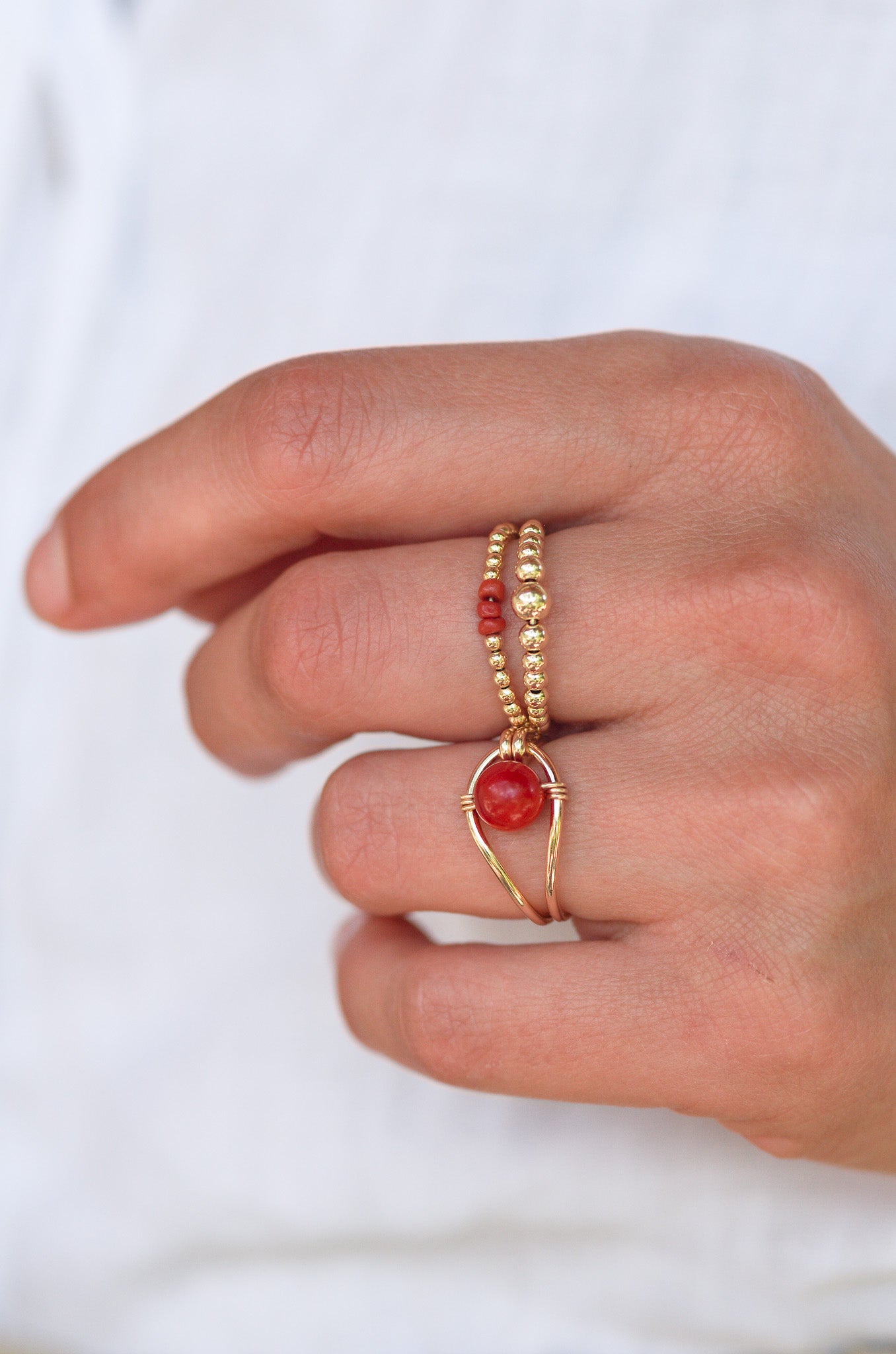Hand wearing Sustainable  gold rings with red coral on a white background