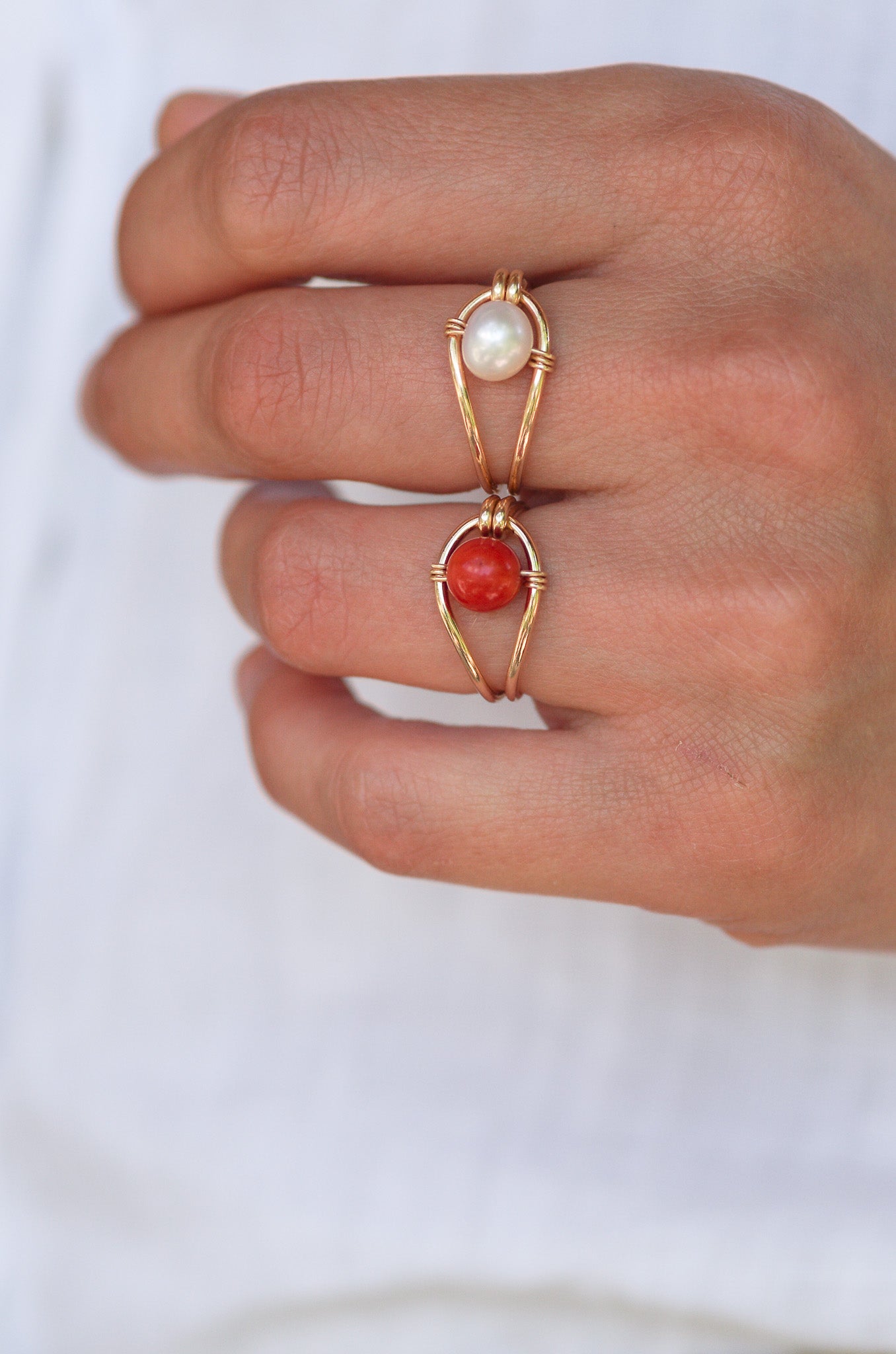 Hand wearing two Sustainable gold rings with pearls and coral on a white background